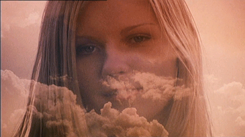 This may contain: a woman with long blonde hair standing in front of clouds