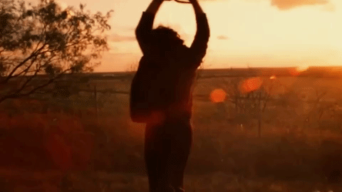 This may contain: a woman standing in the middle of a field with her hands up to the sky