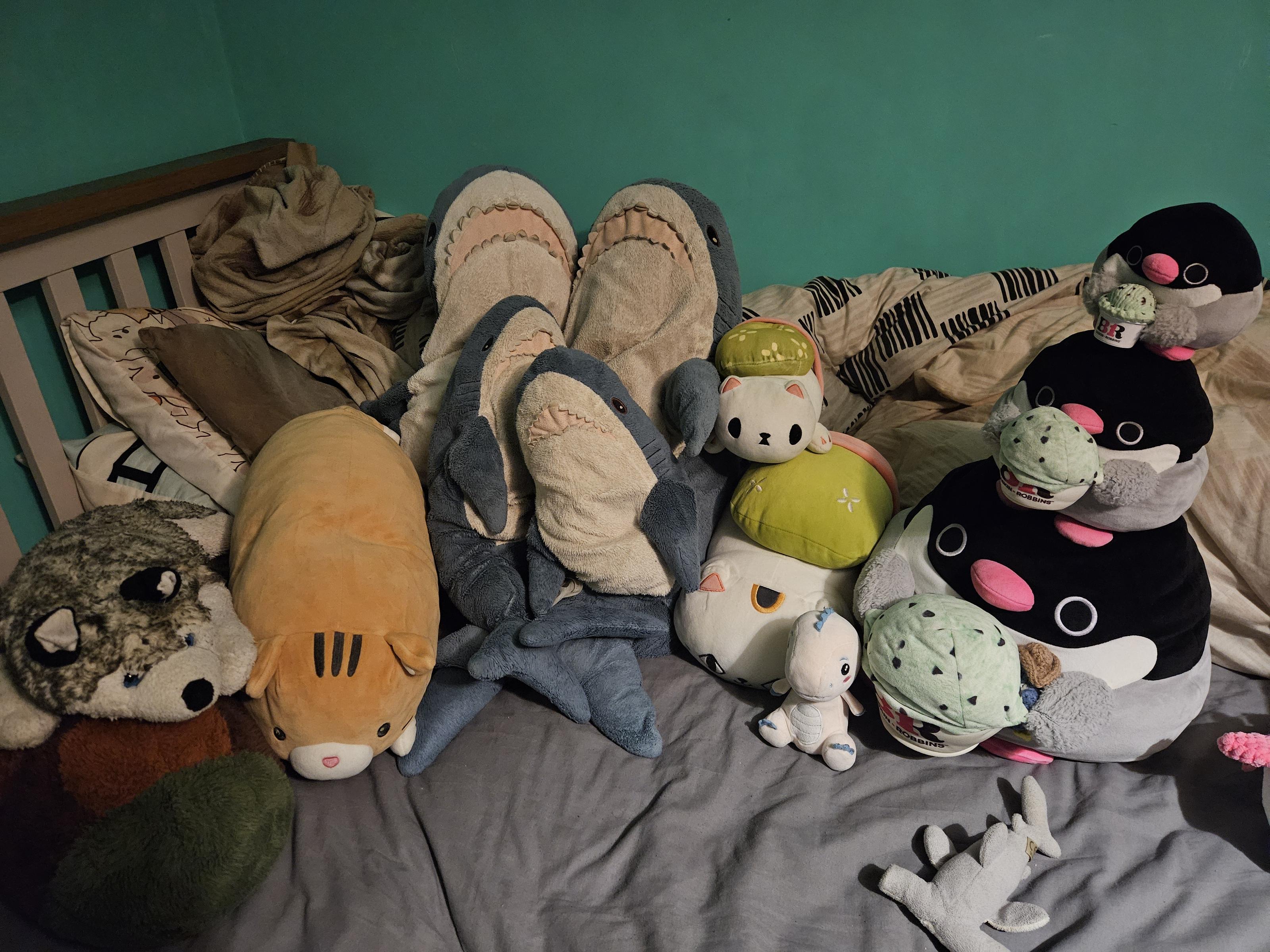 Plush toys from left to right: a turtle, a wolf, a long orange cat , four ikea blahajs two big and two small,two cats with green backpacks one big and one small, a small pink anthro dinosaur,three identical penguins with ice creams in a stack each one smaller then the last and a very tiny hammerhead shark