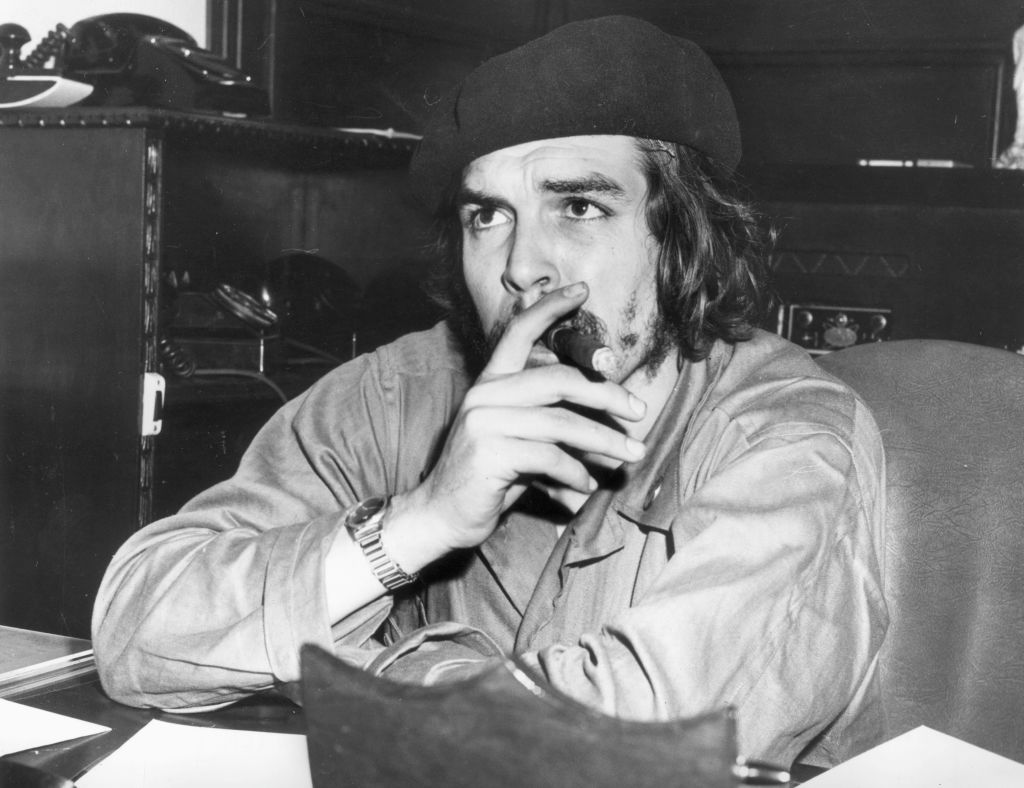 Che Guevara sitting at a desk smoking a cigar.